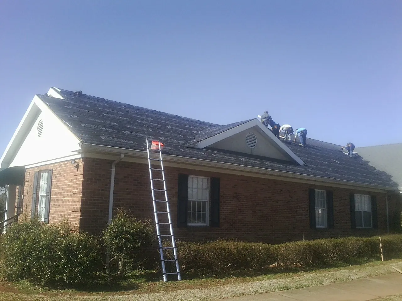 Crew tearing shingles off a brick ranch roof with a ladder set — Emergency Roof Repair work by our crew in Port Washington