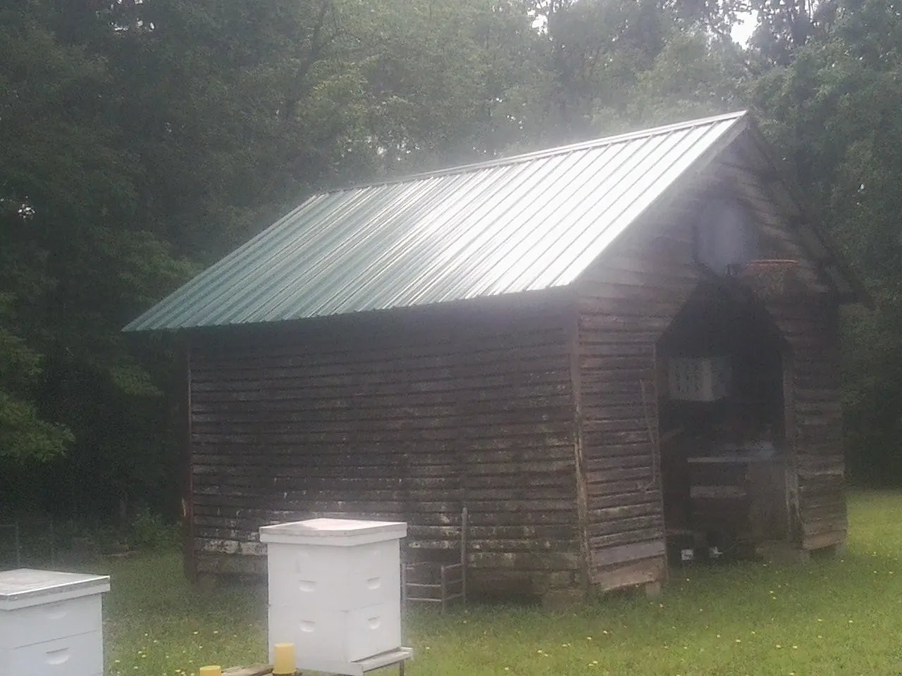 Green metal roof on a weathered barn beside stacked beehives in Port Washington