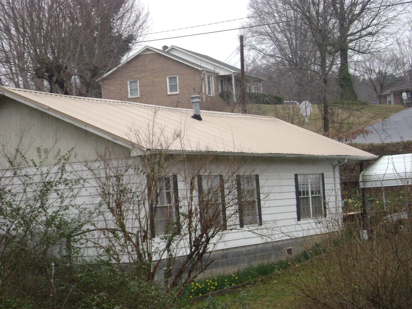 Tan metal roof on a white sided house set into a hillside — Commercial Roofing by Roofing Brothers in Port Washington